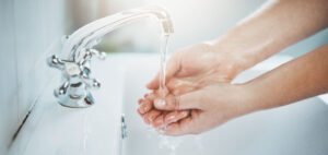 Mains sous un robinet avec écoulement d’eau, illustrant le suivi, la maîtrise et la détection des consommations d’eau dans le logement grâce à des solutions connectées et l'installation de compteurs d'eau individuels dans l'habitat collectif avec OCEA Smart Building